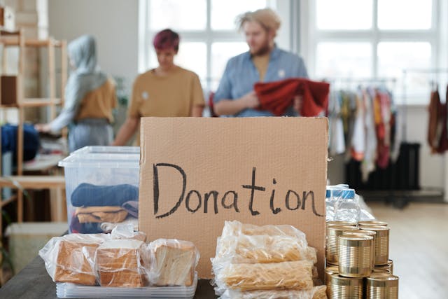 Cardboard box with 'Donation' written on the side in sharpie. Box has canned and other goods around it